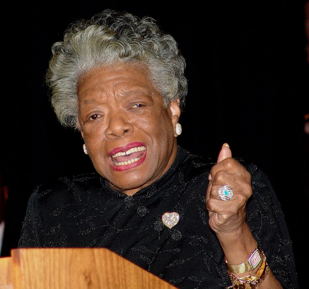 Maya Angelou speaking at a podium with her fist raised as to emphasize what she is saying