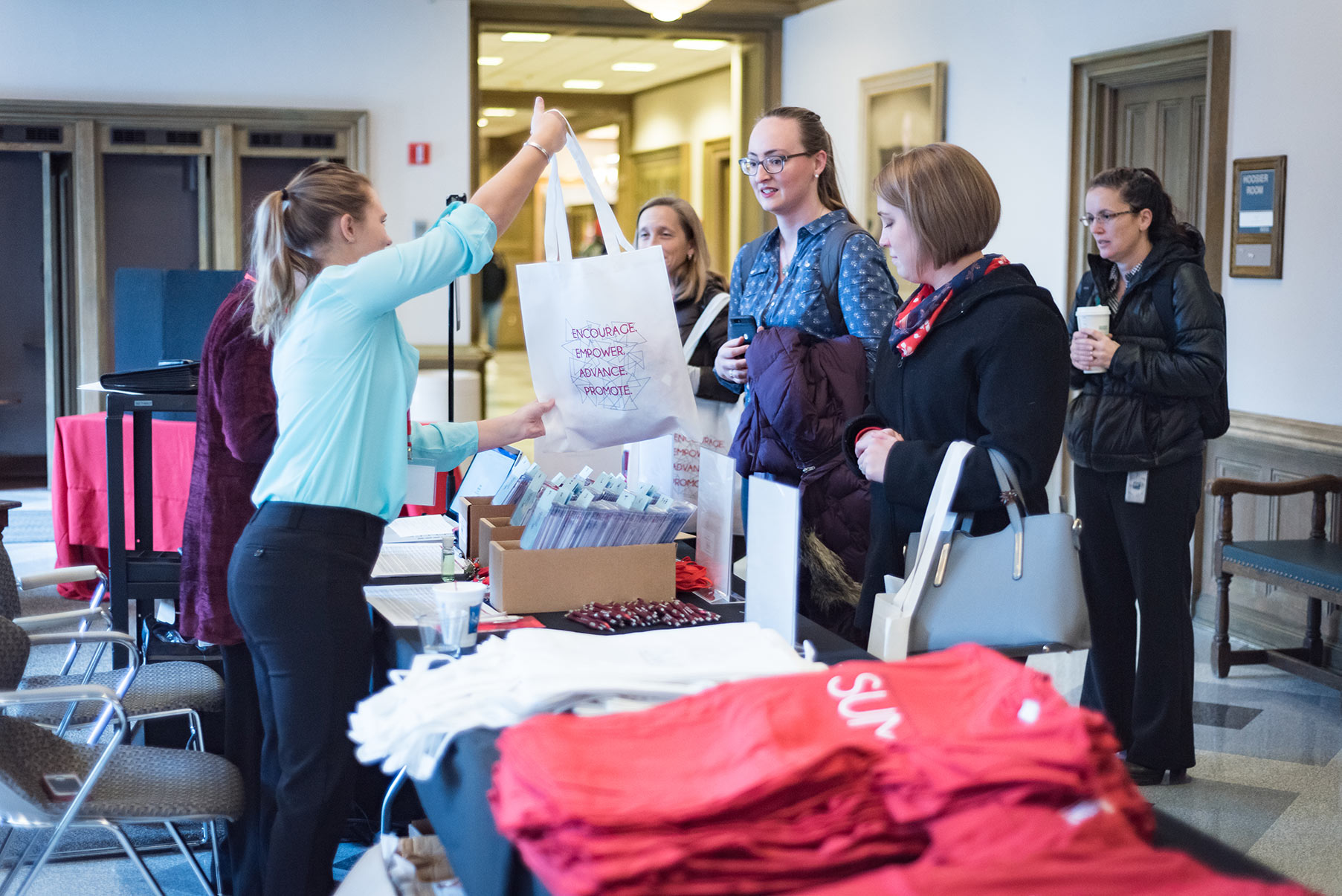 A woman hands over a swag bag to a registrant at the CEW&T conference. The bag has the words Encourage, empower, advance, promote printed on it.